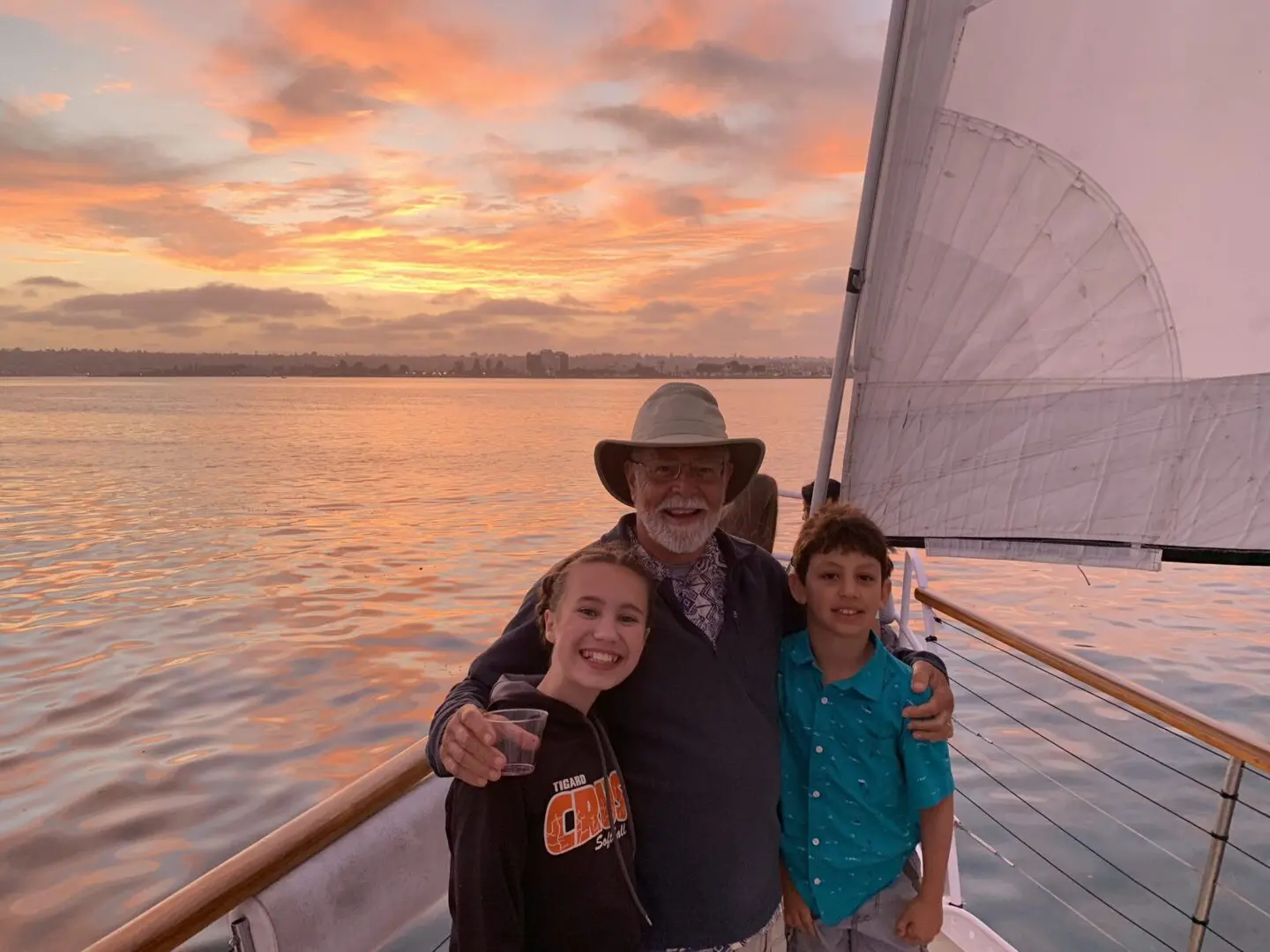 Three people smiling on a boat during a colorful sunset.
