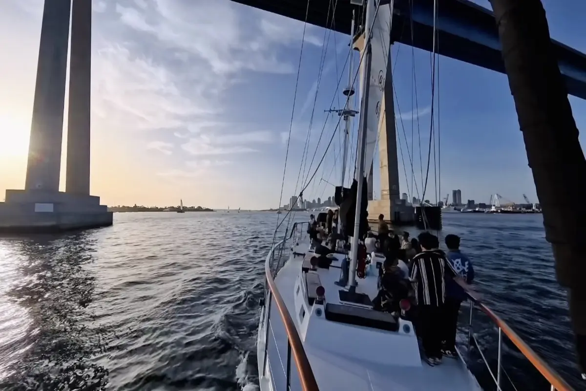 Sailboat gliding under towering bridge at sunset