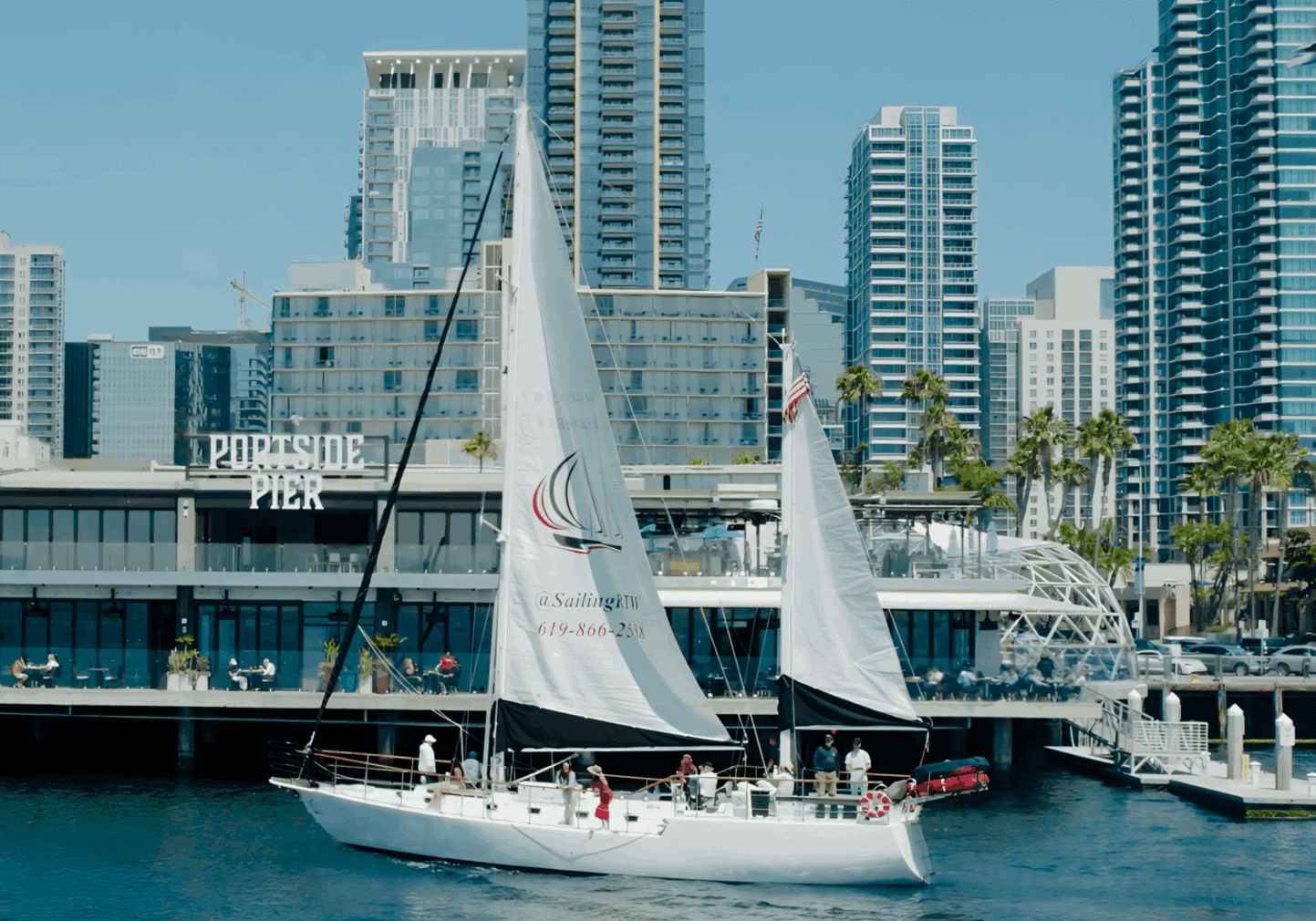 Sailboats gliding near a city waterfront with tall buildings.