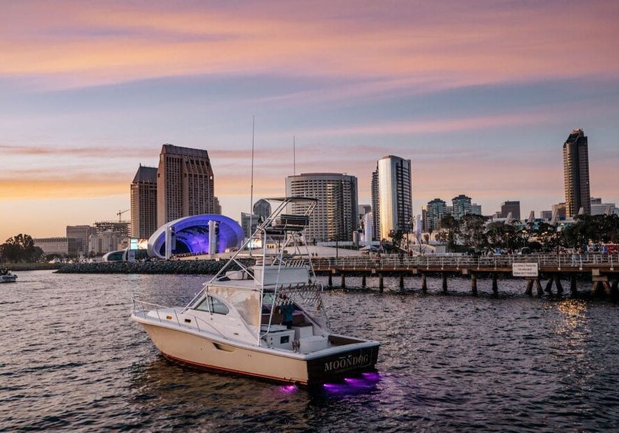 Boat docked near a city skyline at sunset with purple lights.