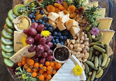 A colorful charcuterie board with fruits, nuts, cheeses, and pickles.
