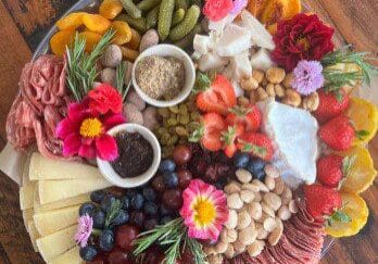 A vibrant charcuterie board with meats, cheeses, fruits, nuts, and edible flowers.