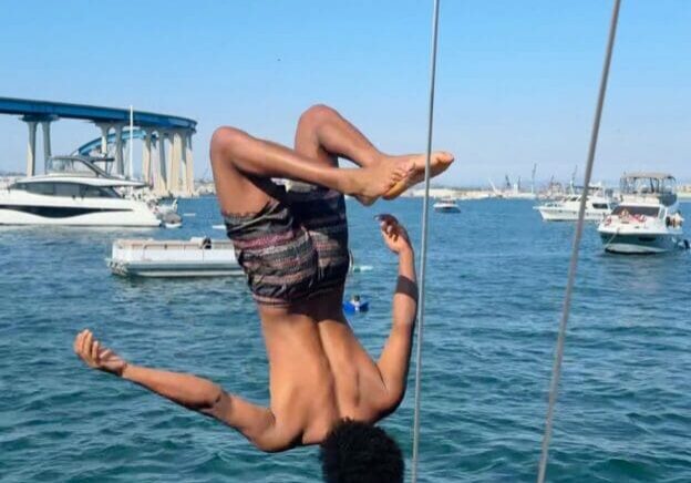 Person mid-flip over water with boats in background.