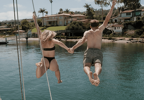 A couple joyfully jumps into a lake holding hands on a sunny day.