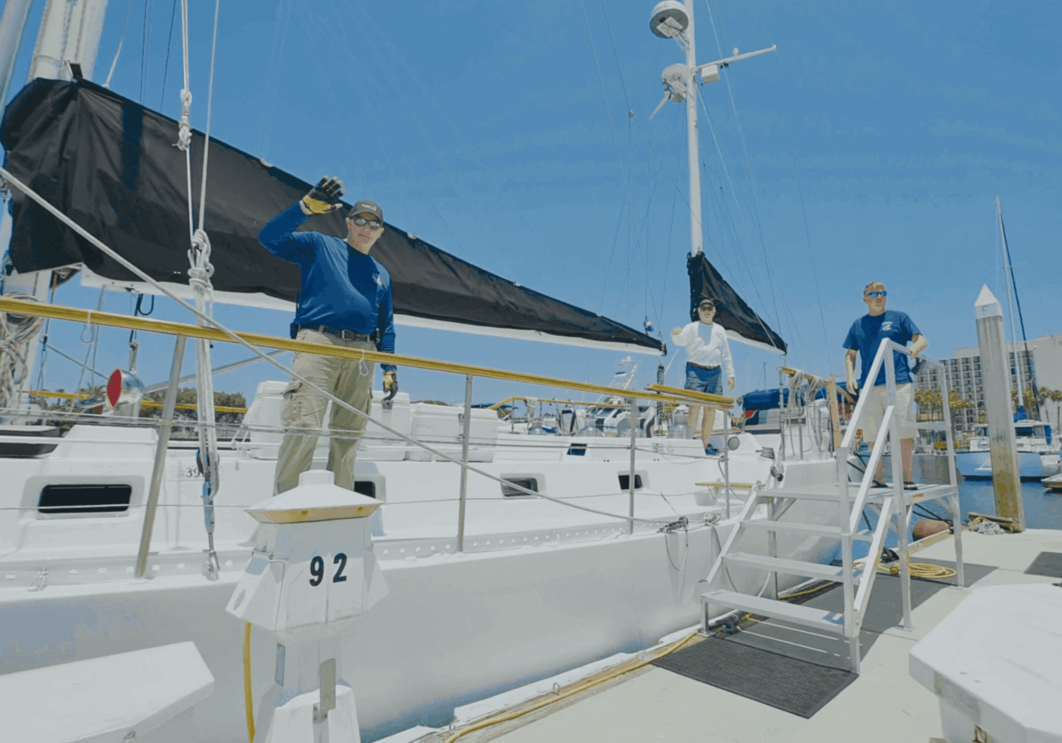 Two men on a docked sailboat preparing for a sail.