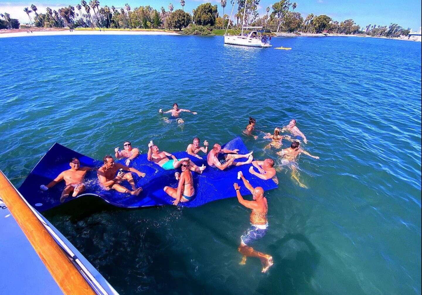 Group of people swimming and lounging on a float in a lake on a sunny day.
