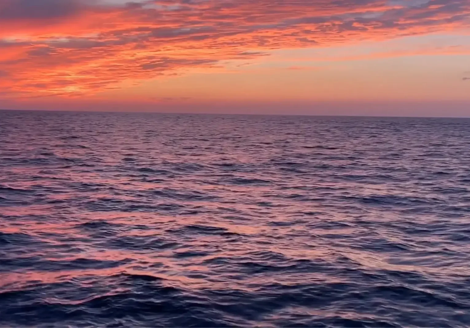Sunset over a calm ocean with colorful sky.