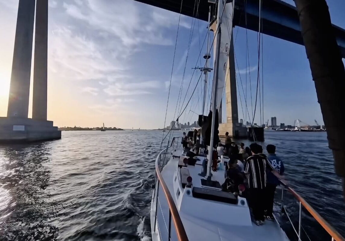 Sailboat gliding under towering bridge at sunset